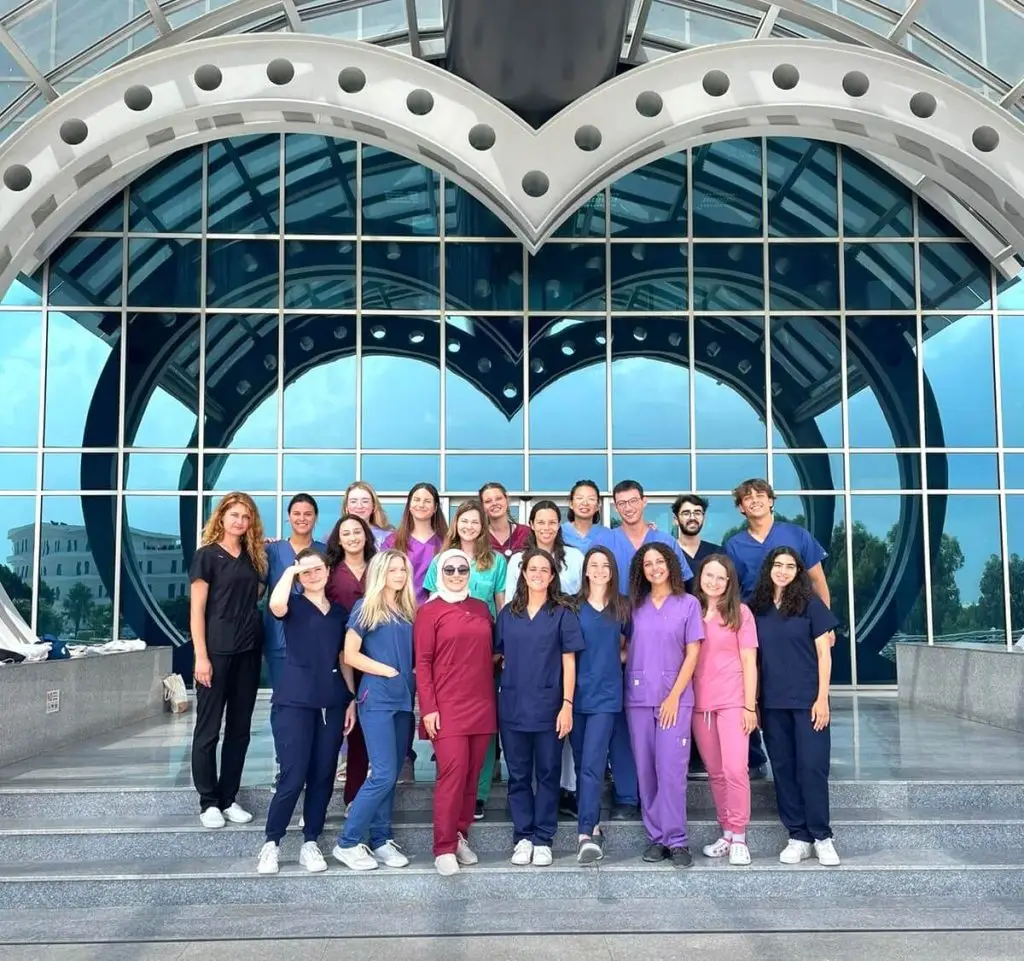 Group of international medical students standing in front of Near East University medical faculty building in North Cyprus, wearing medical uniforms.
