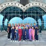 Group of international medical students standing in front of Near East University medical faculty building in North Cyprus, wearing medical uniforms.