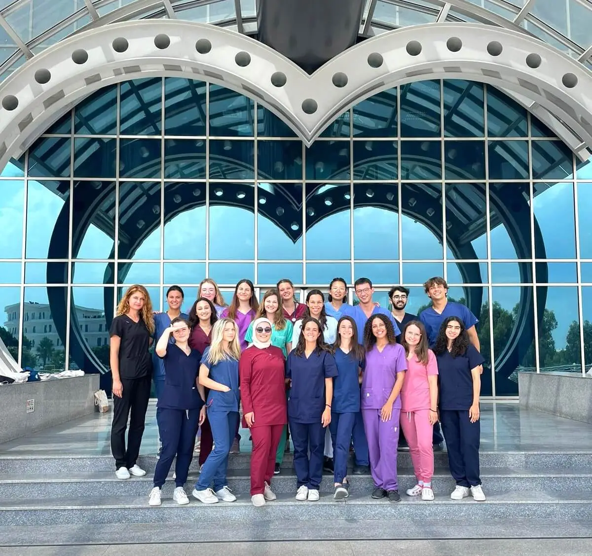 Group of international medical students standing in front of Near East University medical faculty building in North Cyprus, wearing medical uniforms.