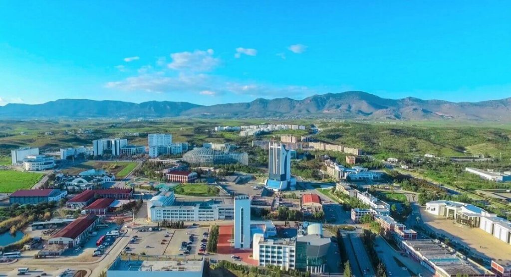 Aerial view of Near East University campus in North Cyprus, featuring modern buildings, green landscape, and surrounding mountains.