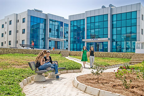 Girne American University campus with students relaxing and walking in front of modern academic buildings, showcasing campus life in North Cyprus.