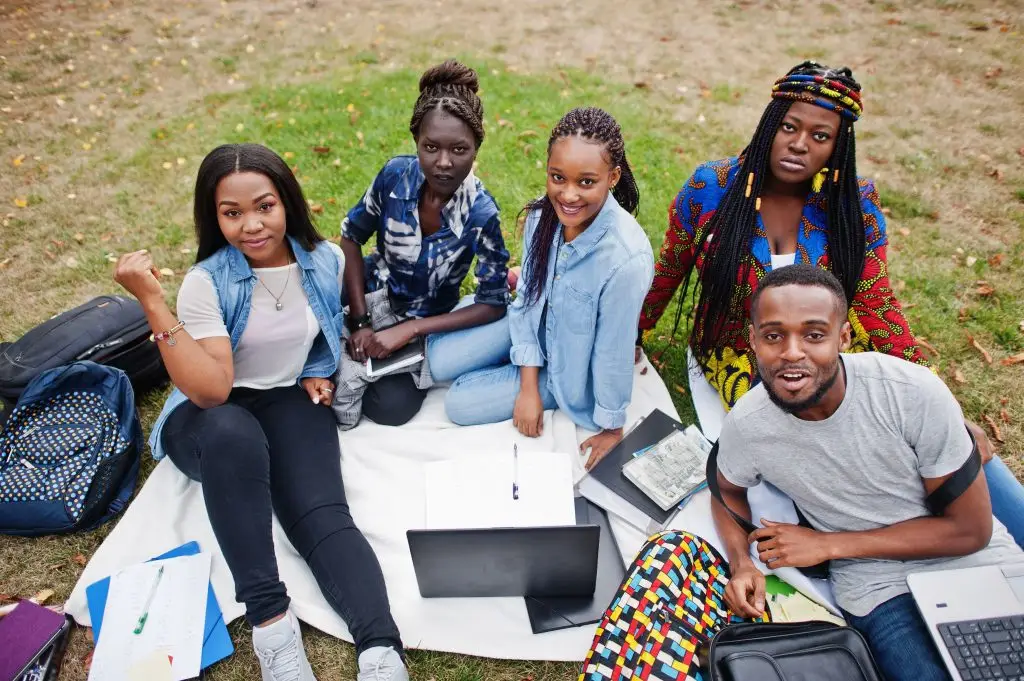 Group of African international students studying together on campus lawn with laptops and notebooks, representing student diversity in North Cyprus universities.