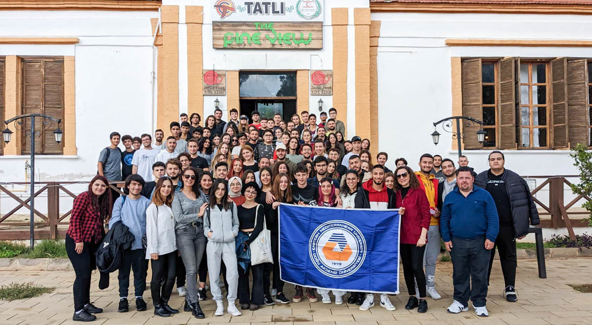 Large group of students from Eastern Mediterranean University (EMU) in North Cyprus holding a university flag during a social activity or field trip.