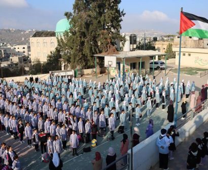Hundreds of Palestinian students in uniform gathered for a morning assembly at a school courtyard with the Palestinian flag raised high.
