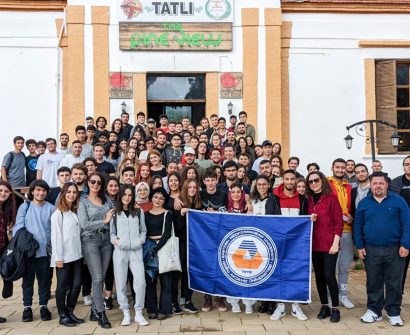 Large group of students from Eastern Mediterranean University (EMU) in North Cyprus holding a university flag during a social activity or field trip.